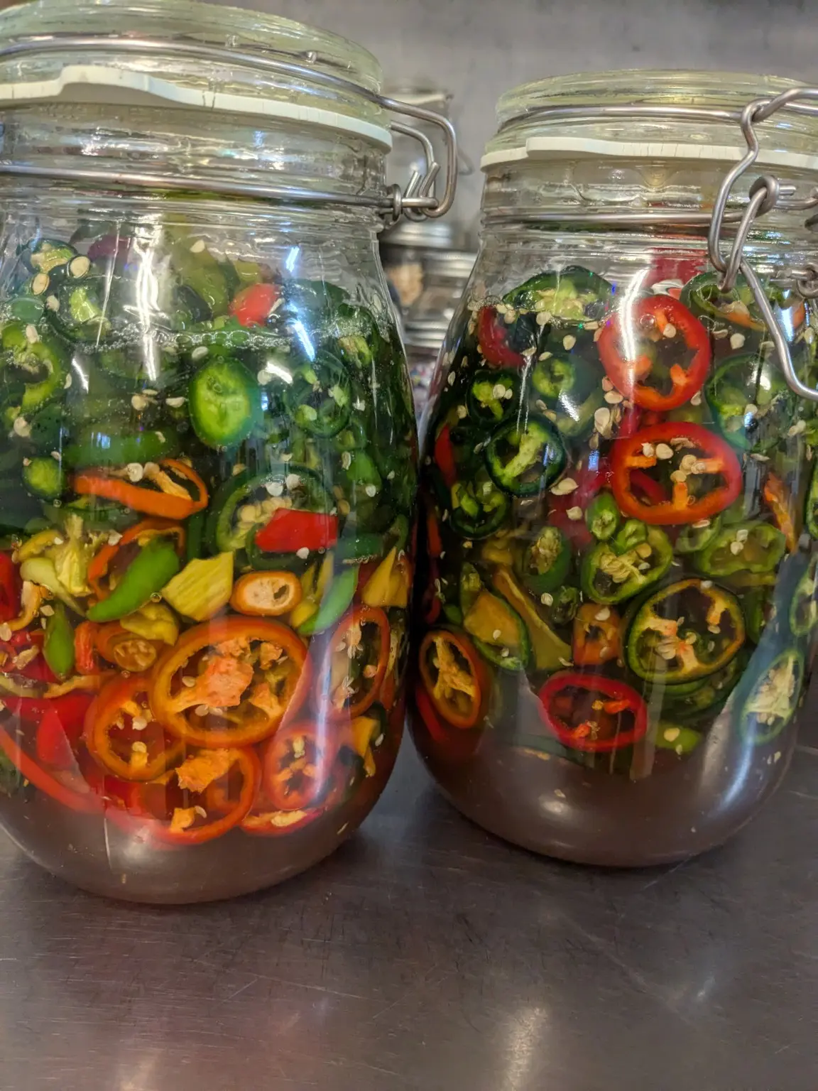 Large jars of colourful peppers preserving in brine